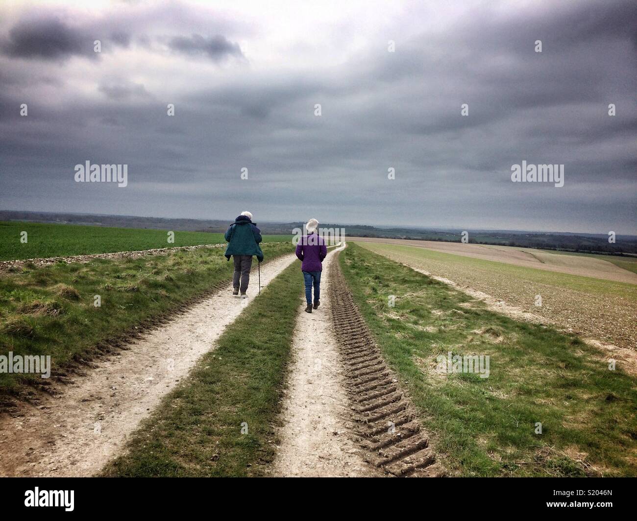 A father and son, both grey haired, hiking a path through farmland in Hampshire, England, UK in overcast weather in early spring. - Smartphone Captured Stock Image