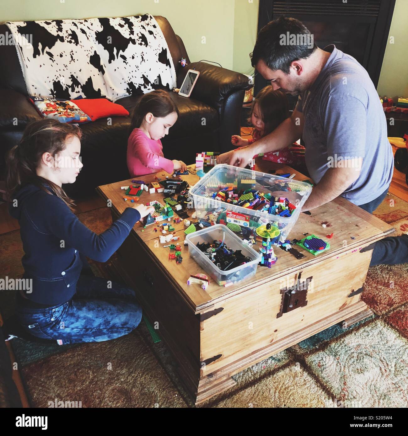 Candid lifestyle image of father playing LEGO with three daughters on a wooden table - Smartphone Captured Stock Image
