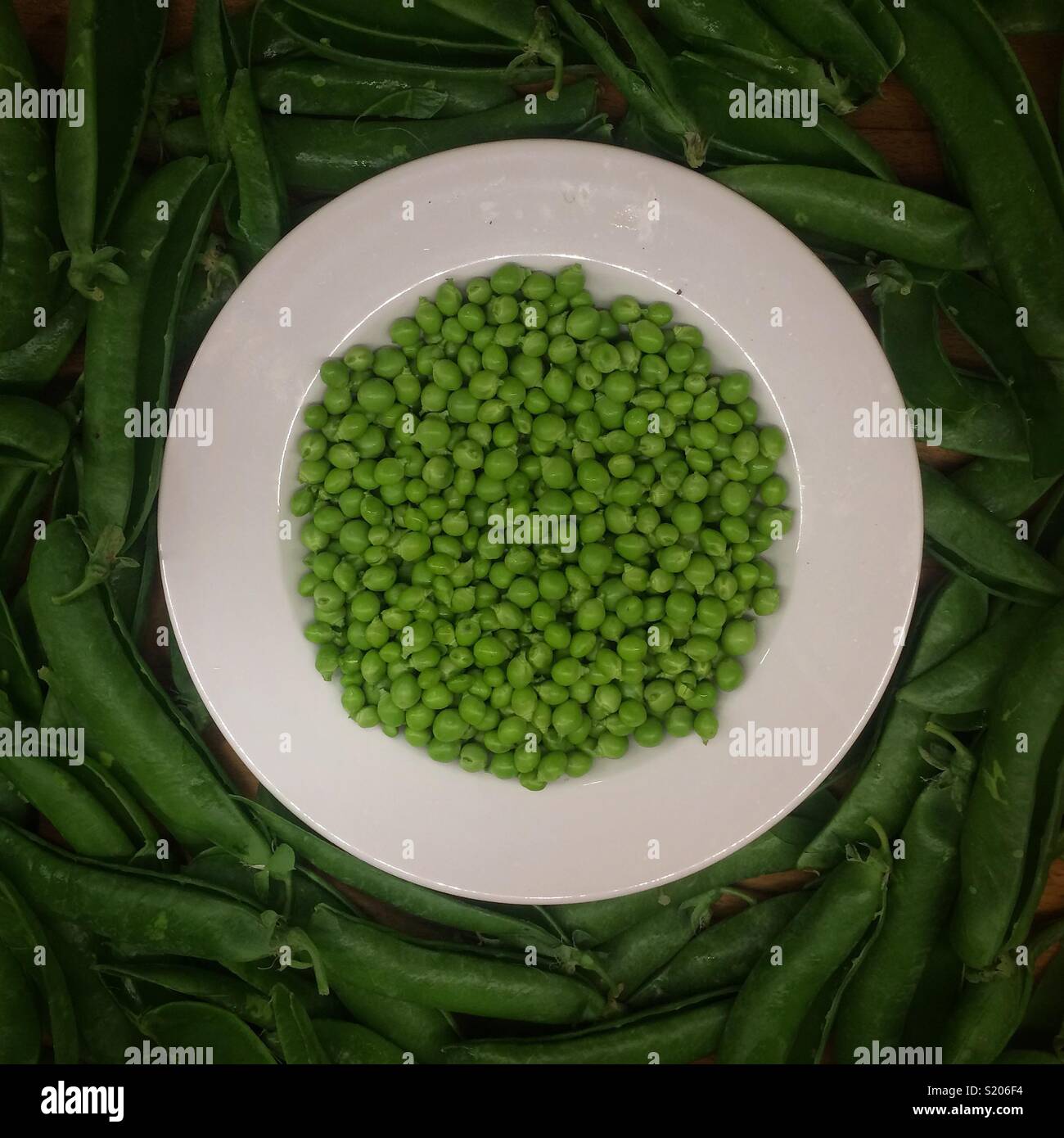 Pods of green peas with leaves on white plate. - Smartphone Captured Stock Image