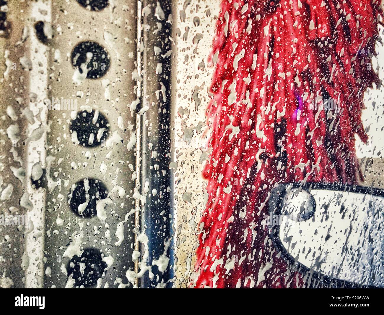 Car wash brush with soap bubbles on window and car mirror in car wash