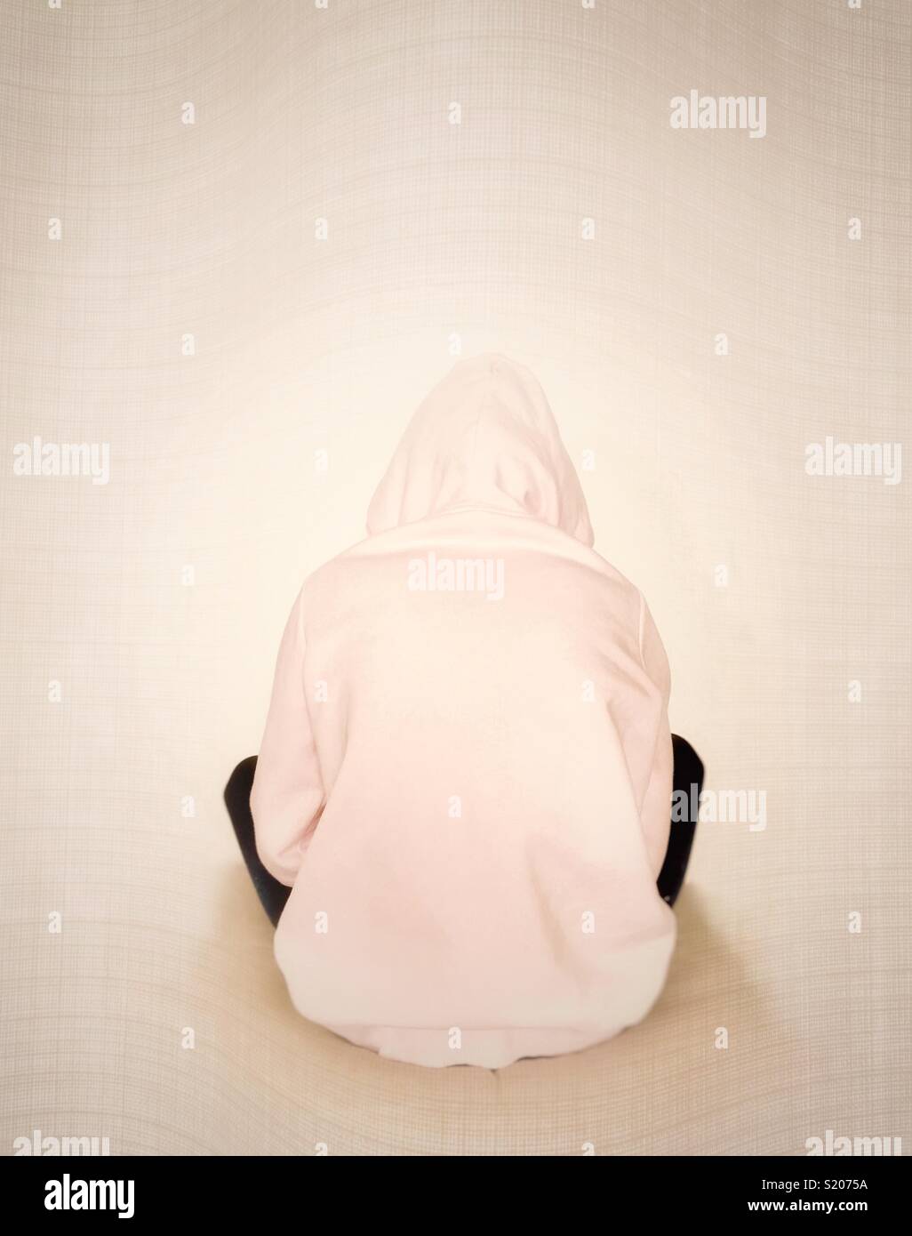 Young girl in pink hoody with back to camera and facing wall. Stock Photo