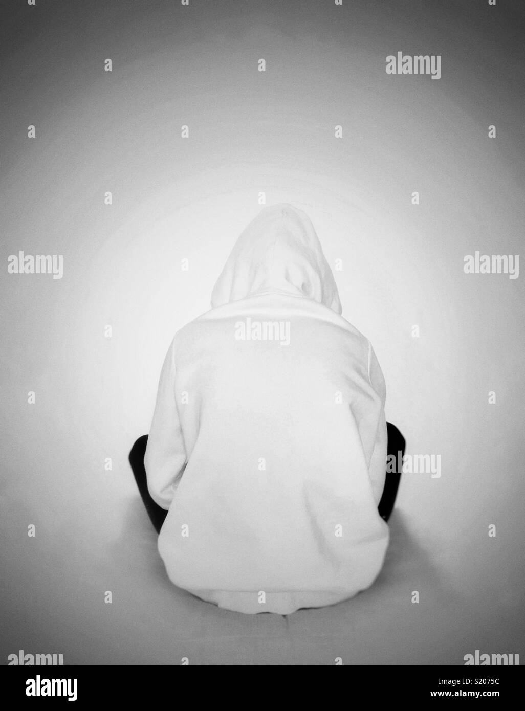 Young girl wearing a hoody facing wall with back to camera Stock Photo
