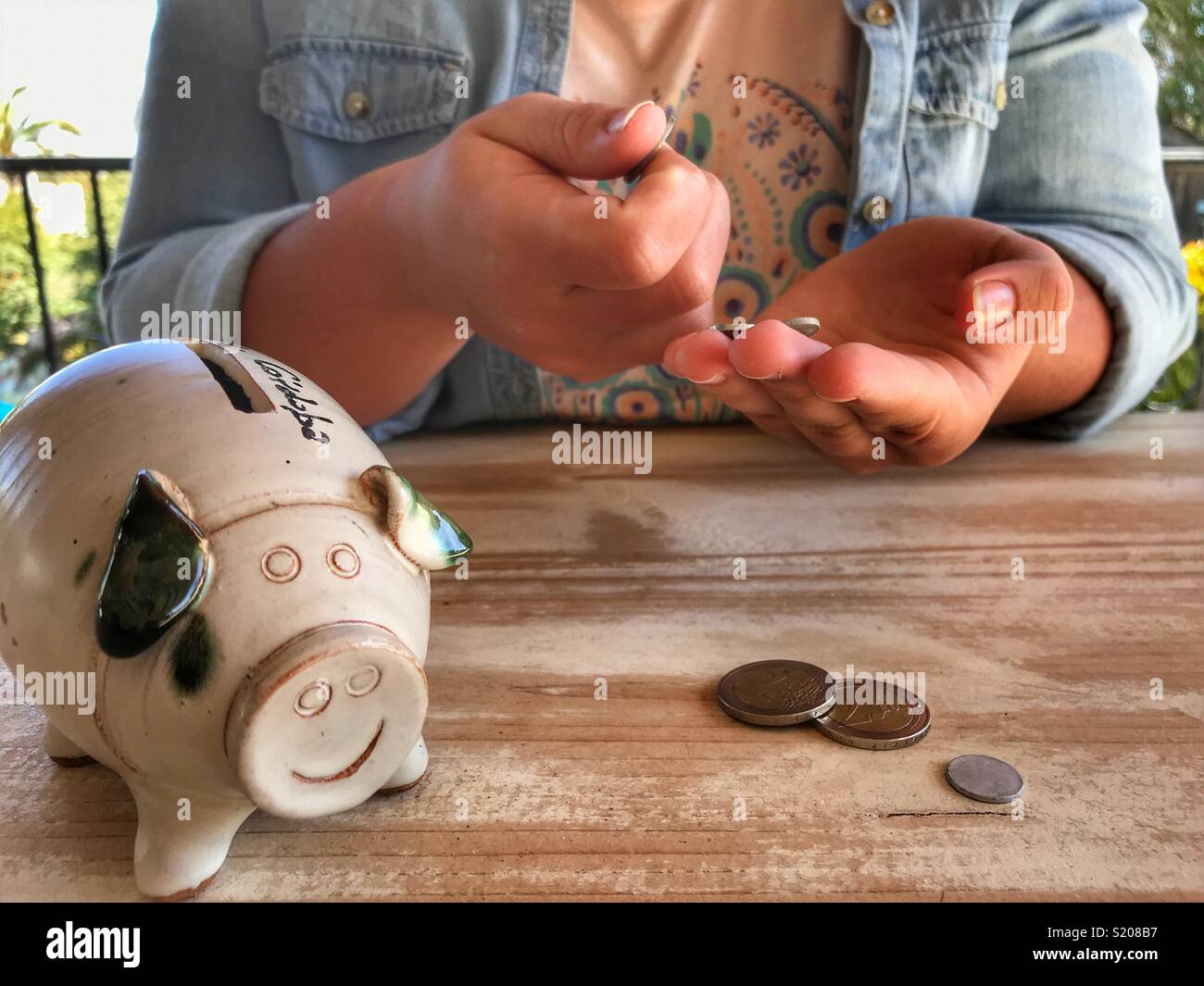 Millennial woman sitting at a table with coins and a piggy bank, midsection - Smartphone Captured Stock Image
