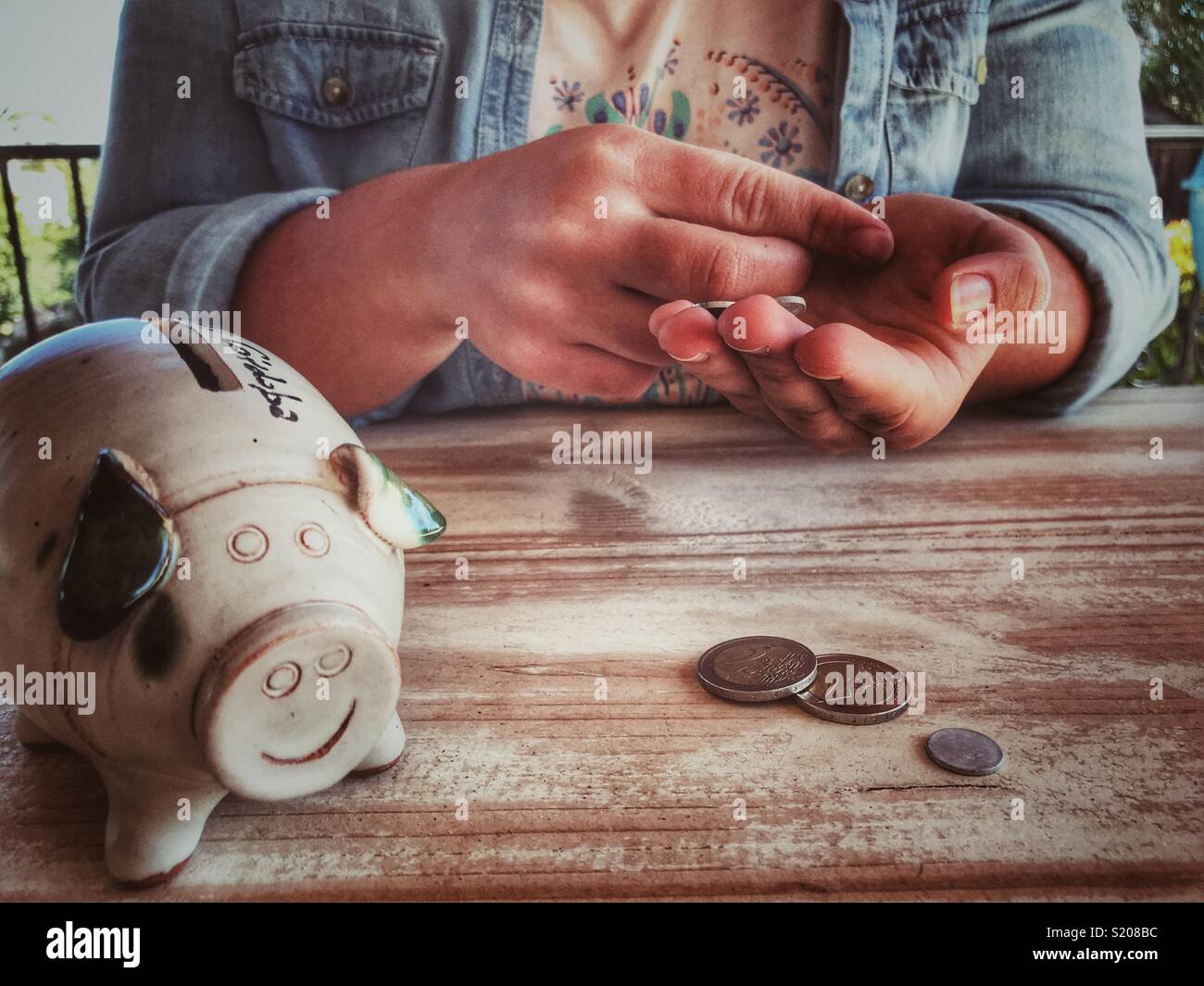 Millennial woman sitting at a table with coins and a piggy bank, midsection - Smartphone Captured Stock Image
