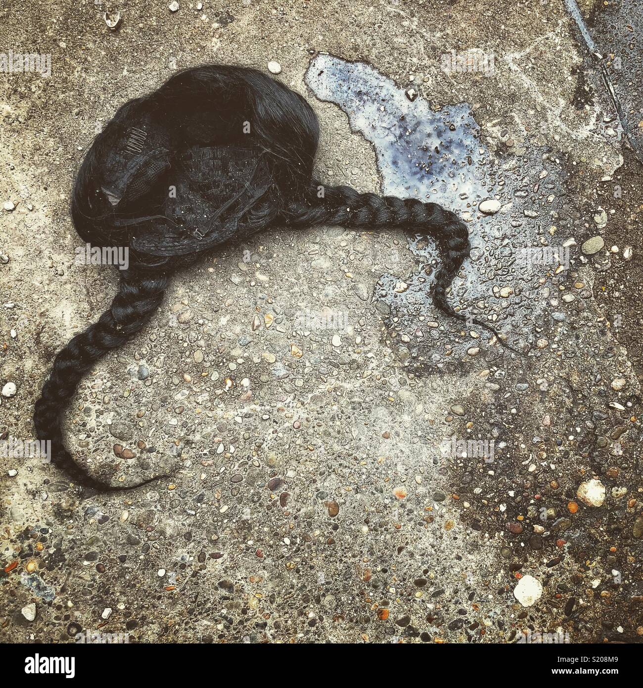 An unusual photo of a black wig with braided pig tails discarded and lying on the sidewalk Stock Photo