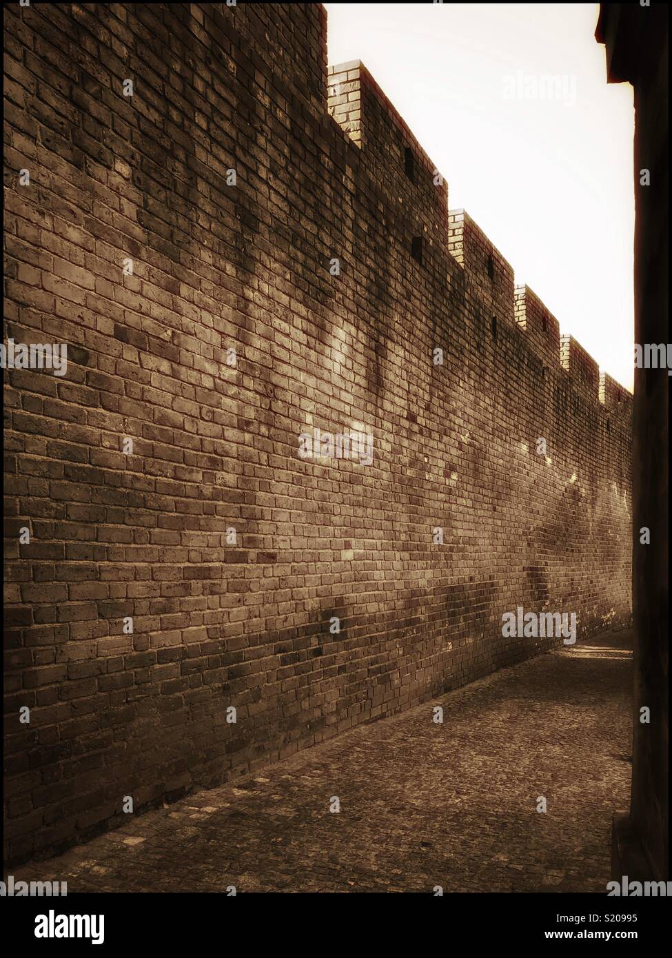 A tall brick wall protects an alley way going to “who knows where...” Mystery, loneliness, abandonment, or maybe friends and smiling faces just round the corner? Photo Credit - © COLIN HOSKINS. - Smartphone Captured Stock Image