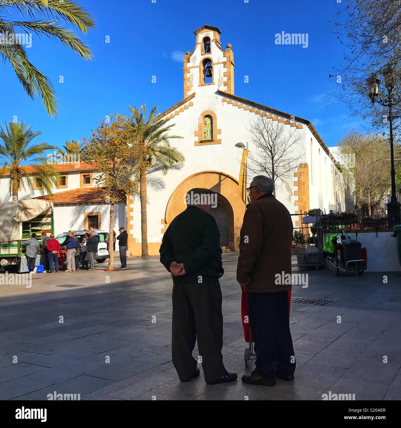 Silhouette of old men talking in a square on market day, in the Old Town of Javea on the Costa Blanca, Spain - Smartphone Captured Stock Image