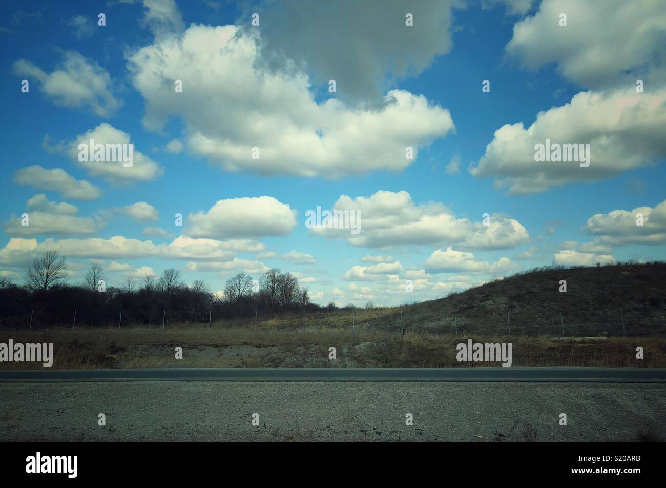 White fluffy cumulus clouds in blue sky view from a road - Smartphone Captured Stock Image