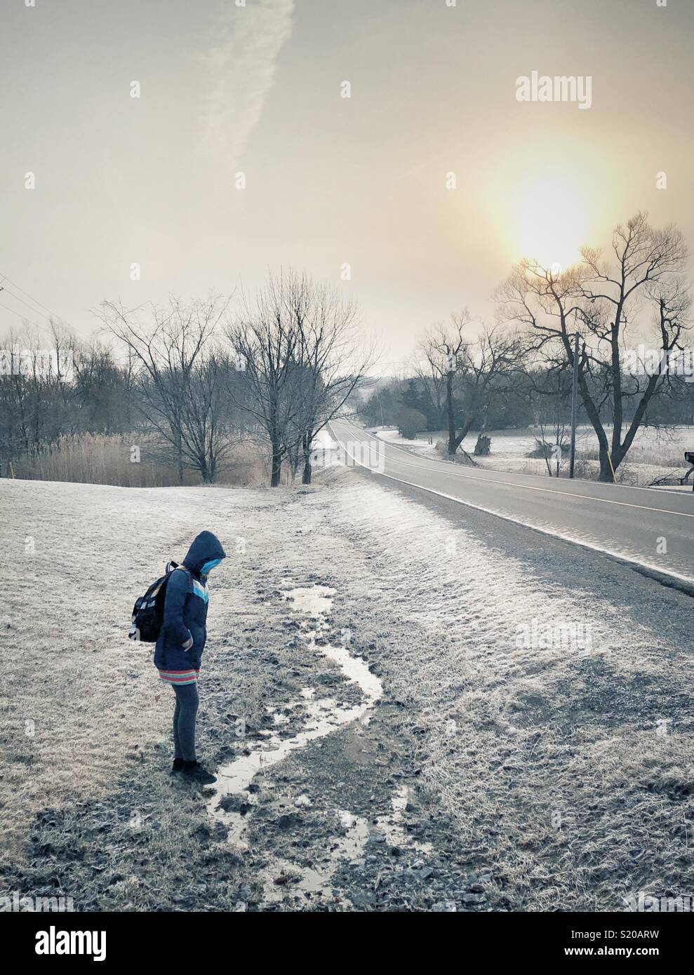 Schoolgirl waiting for bus on rural road in morning during frosty cold weather - Smartphone Captured Stock Image