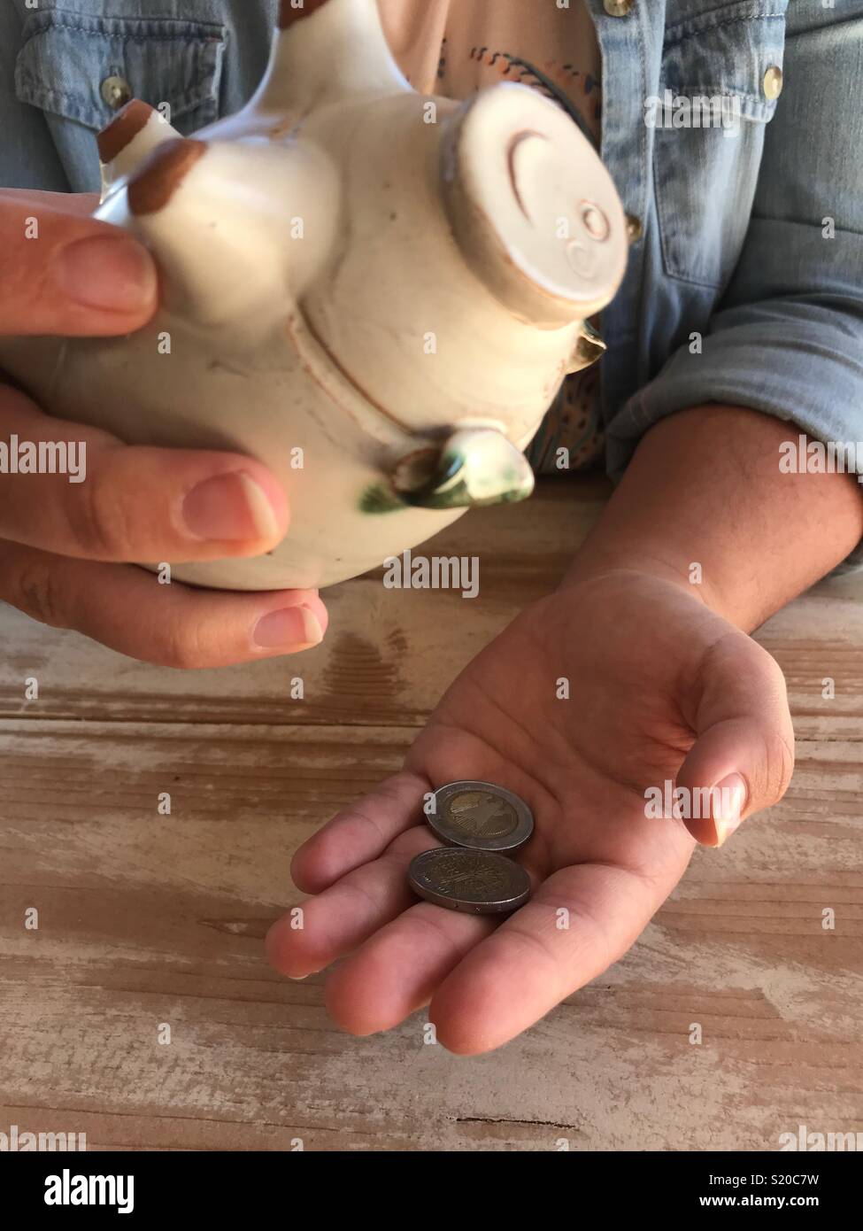 Millennial woman, shaking coins out of a piggyback - Smartphone Captured Stock Image