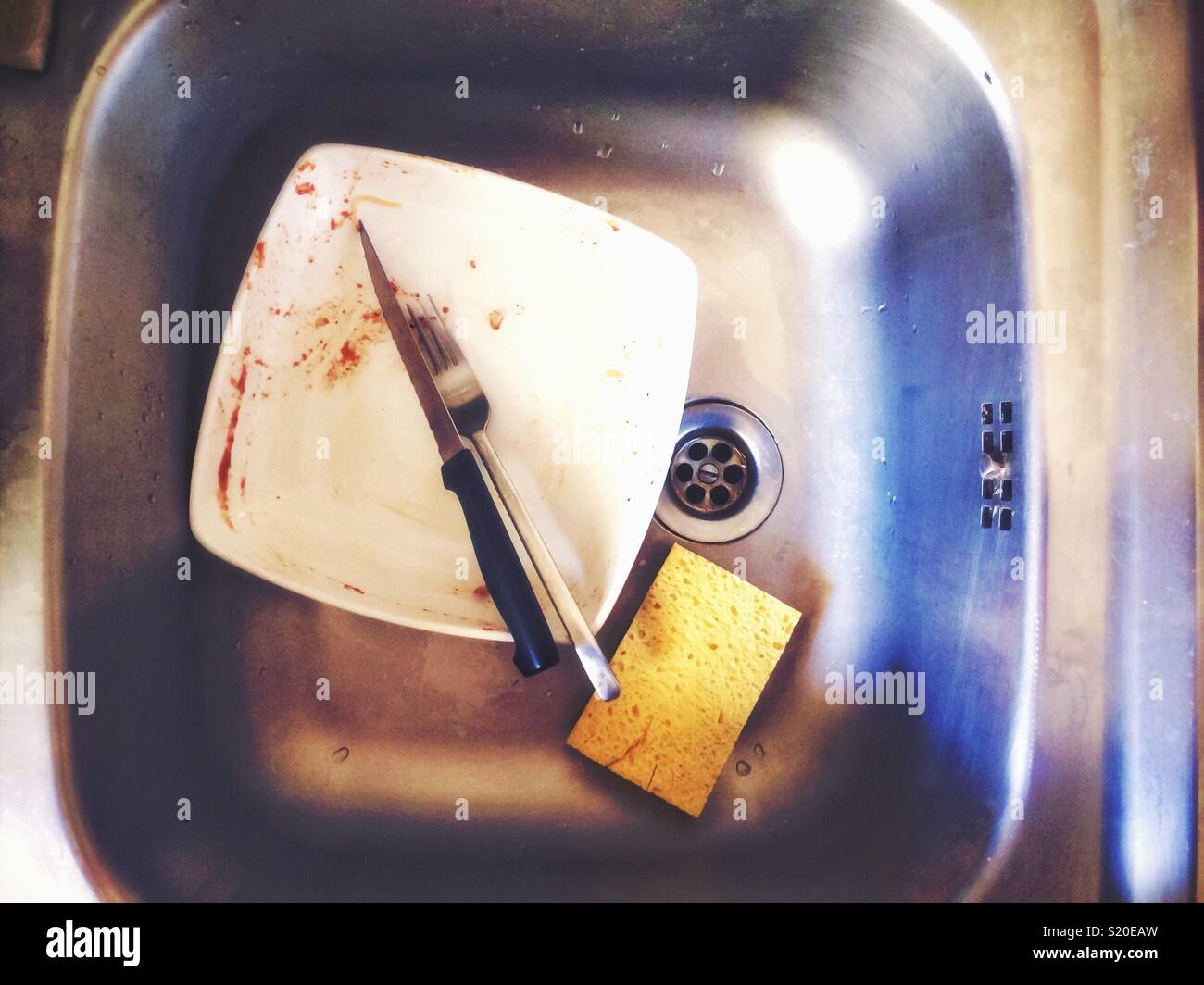 Time to wash the dish, dirty plate in a sink with fork and knife and a sponge. Kitchen and food concept. - Smartphone Captured Stock Image