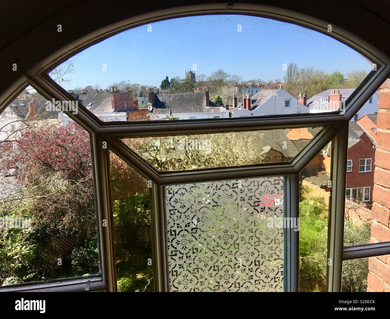 Arched window with etched glass overlooking English gardens and roofs - Smartphone Captured Stock Image