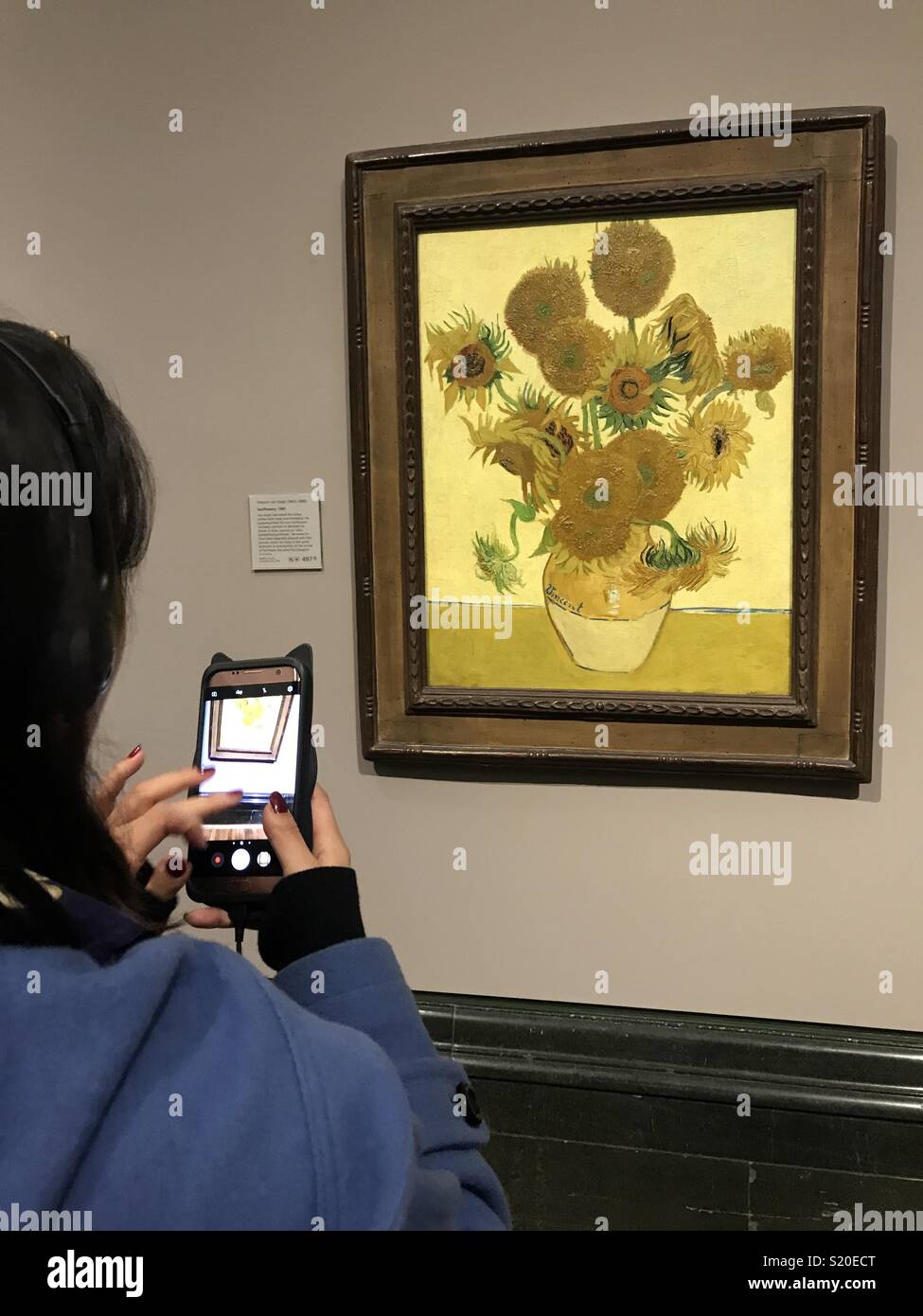 A lady using her mobile phone to take a picture of Vincent Van Gogh's sunflowers Stock Photo