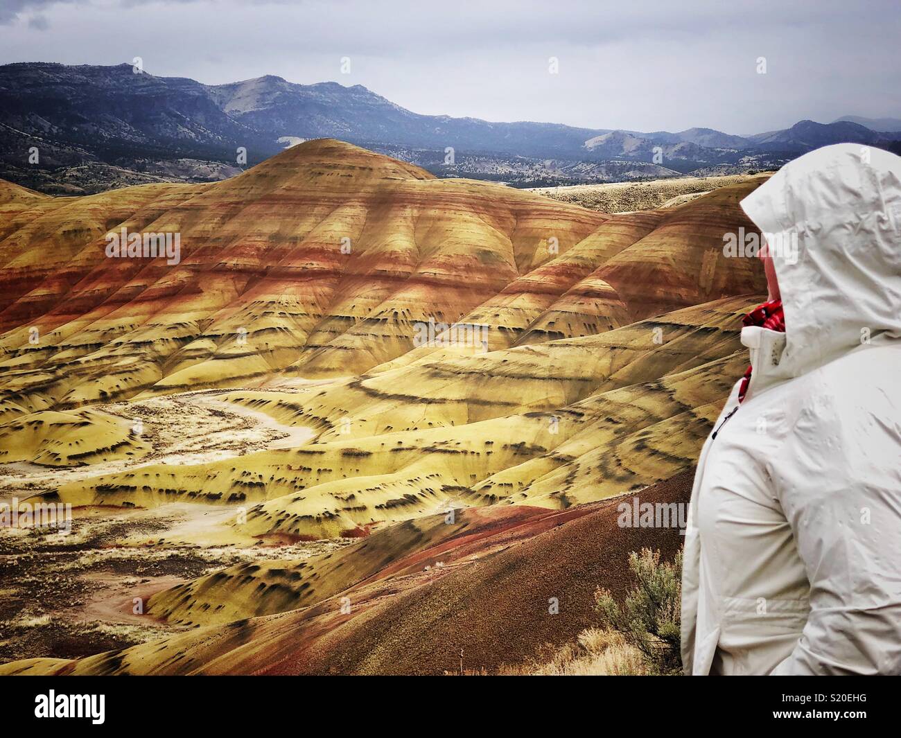Woman in white raincoat admires panoramic view of Painted Hills in Oregon Stock Photo
