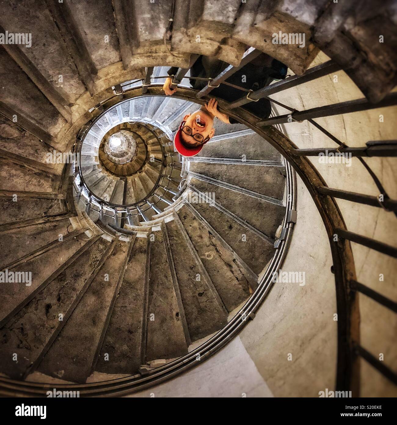 Boy leaning over the bannister on a tight spiral stone staircase taken from below Stock Photo