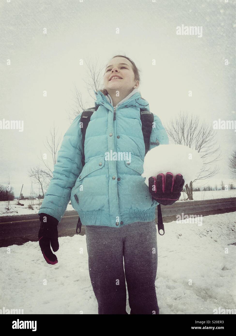 Girl smiling while holding a large snowball outside on an overcast winter day - Smartphone Captured Stock Image