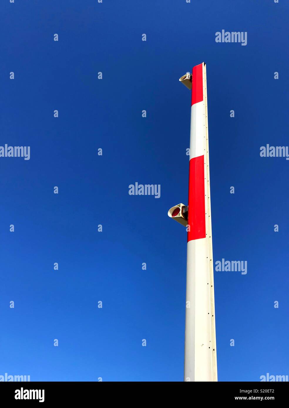 Raised arm of a railway crossing barrier against a deep blue sky - Smartphone Captured Stock Image