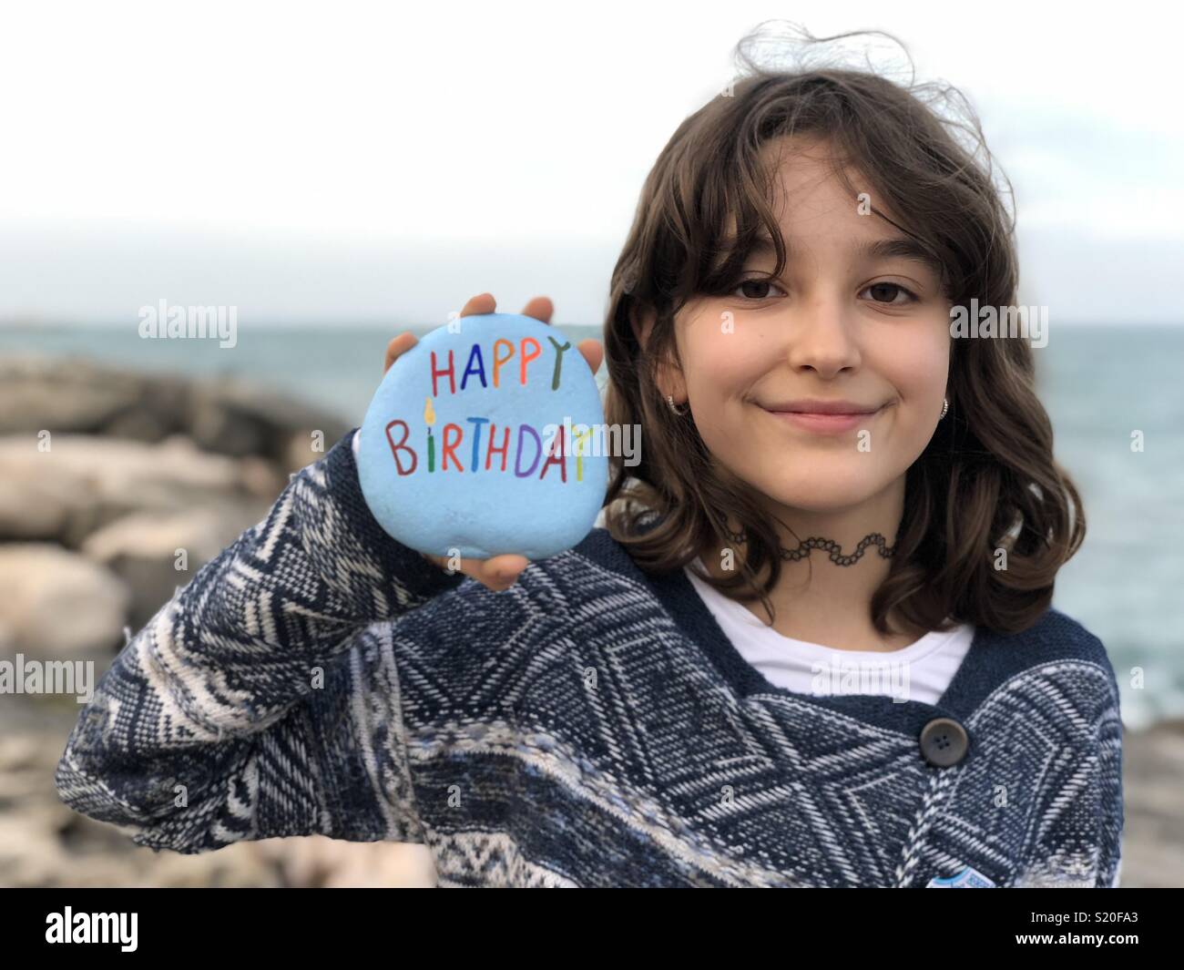 Young girl holding a happy birthday stone with sea background Stock Photo