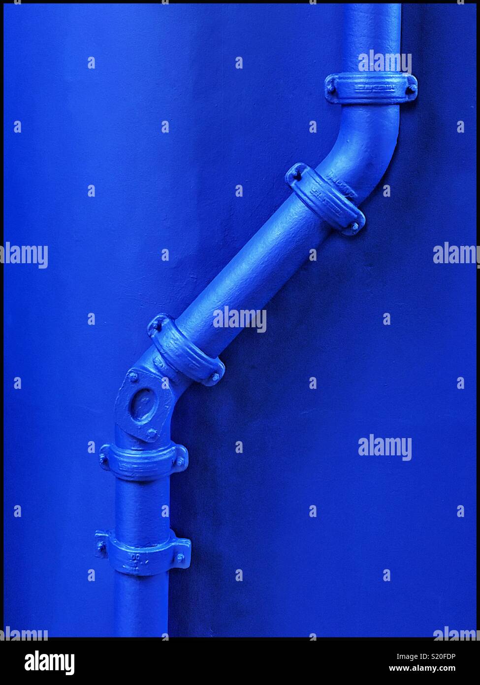 Blue pipes clamped together against a blue wall. A lone colour