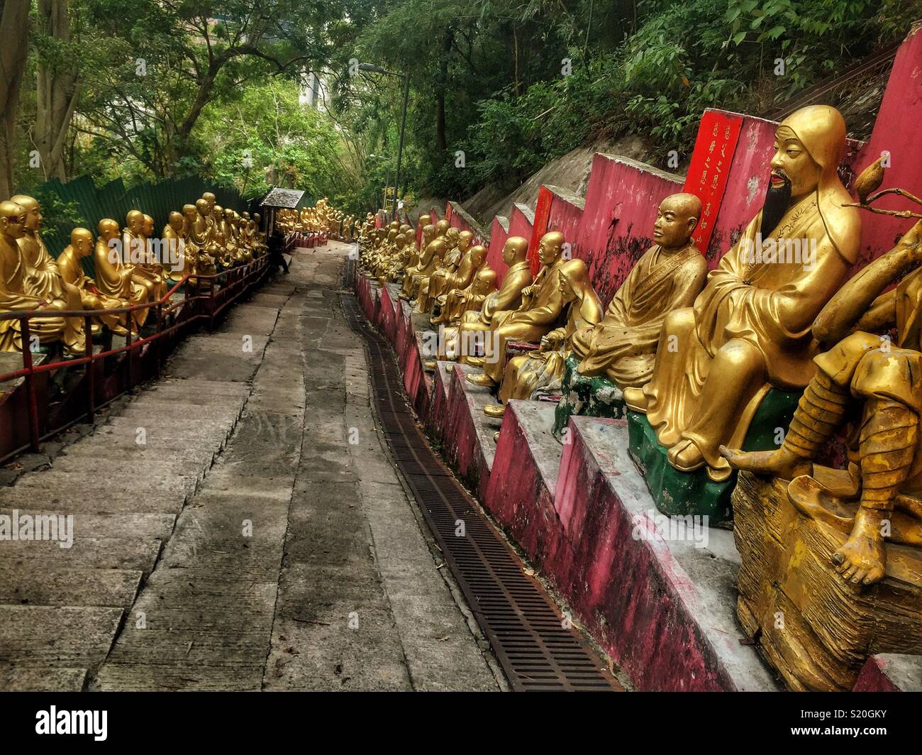 Golden statues of Buddhist 'arhats' line the path leading to the Ten Thousand Buddhas Monastery in Sha Tin, New Territories, Hong Kong - Smartphone Captured Stock Image