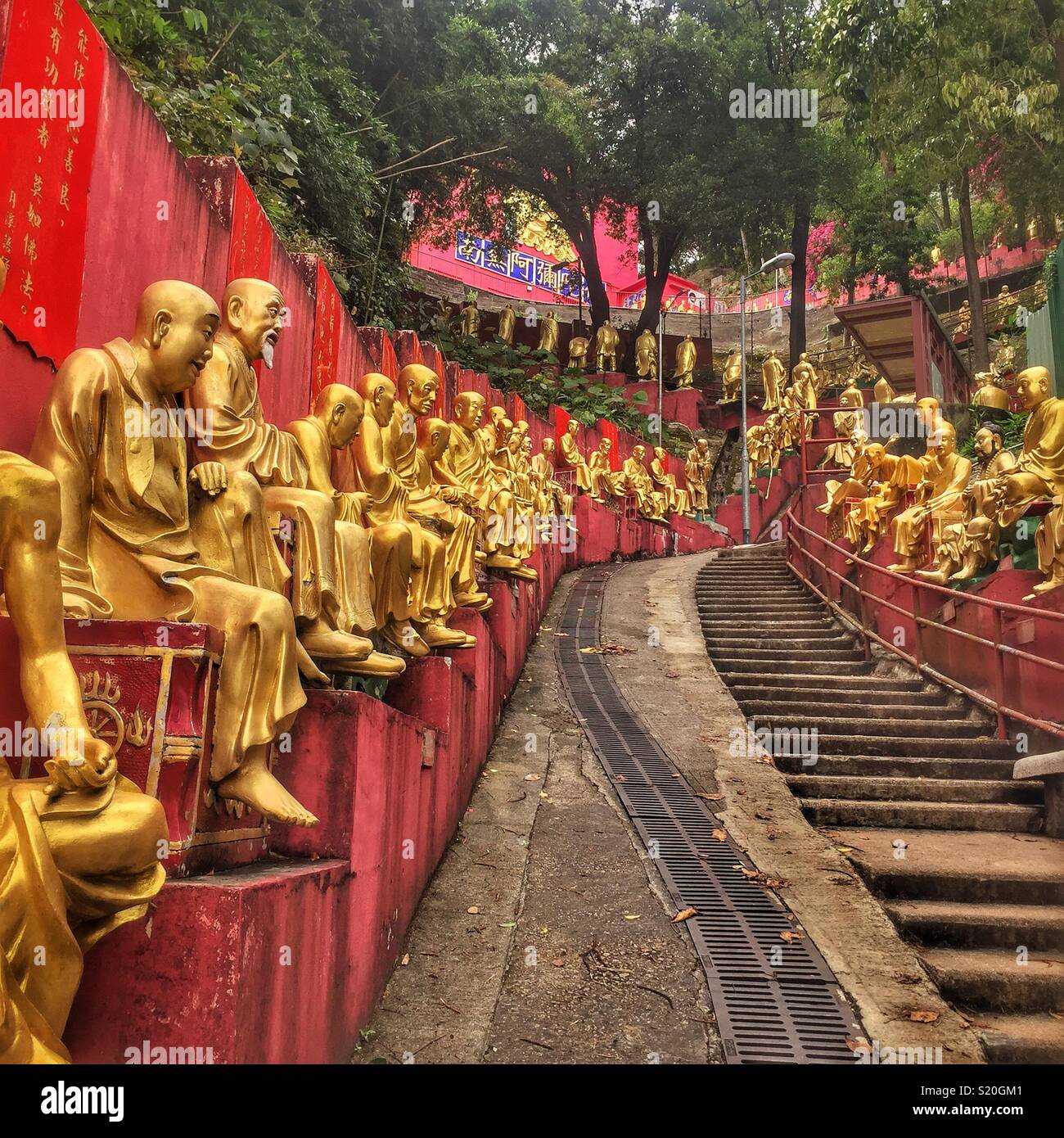 Golden statues of Buddhist 'arhats' line the path leading to the Ten Thousand Buddhas Monastery in Sha Tin, New Territories, Hong Kong - Smartphone Captured Stock Image
