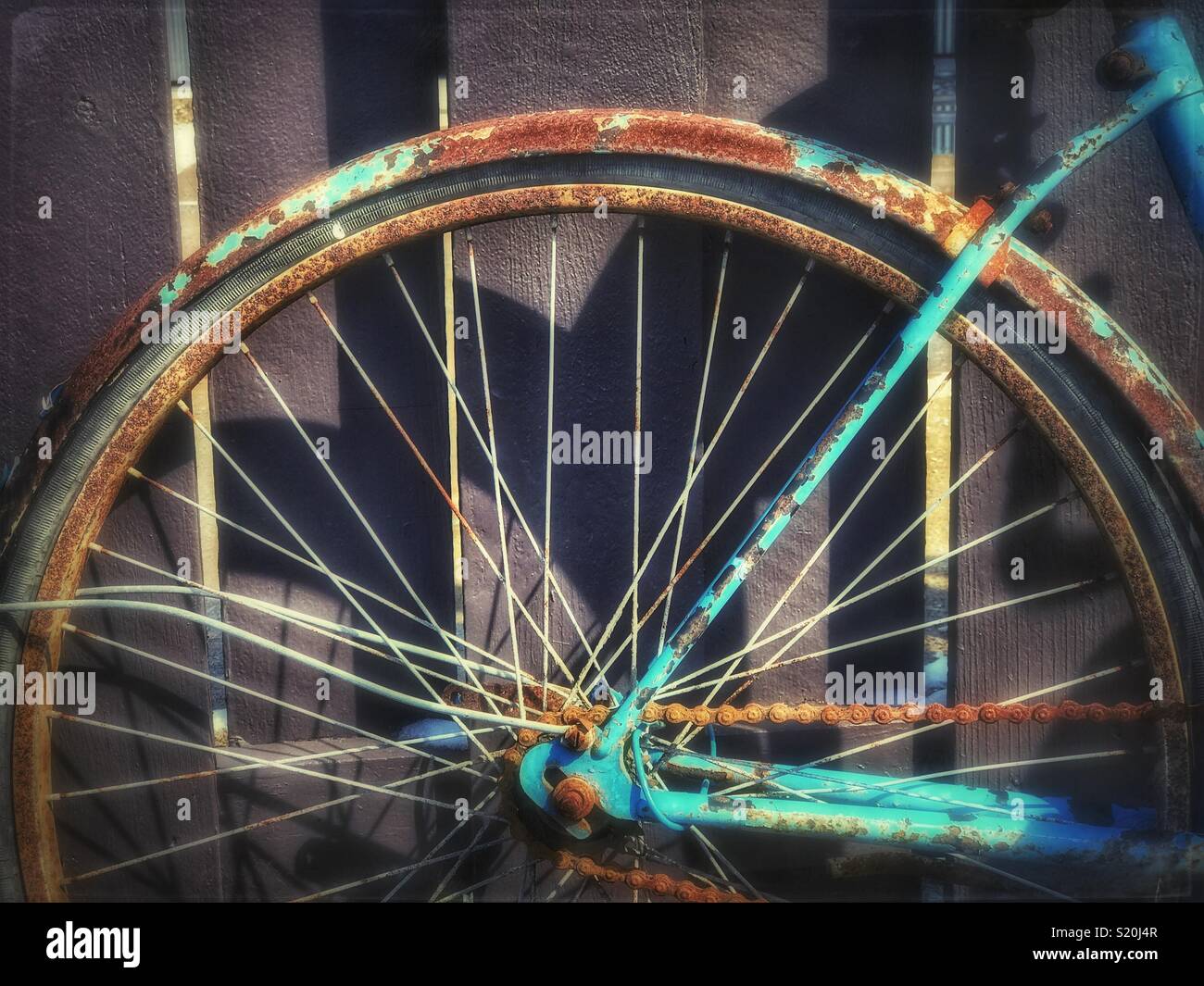 Old rusted blue bicycle wheel against a fence Stock Photo