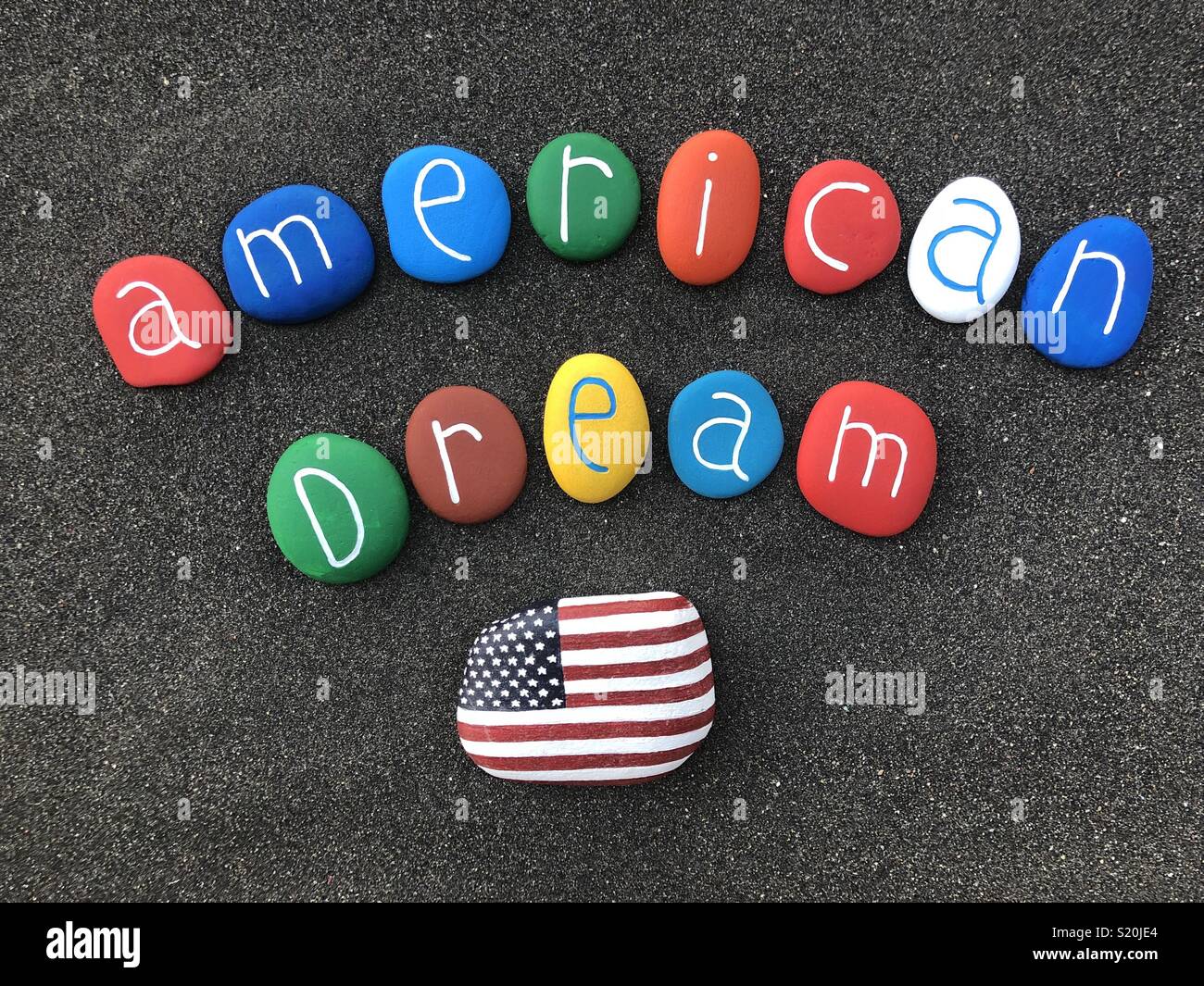 American dream text with multicolored painted sea stones over volcanic sand Stock Photo