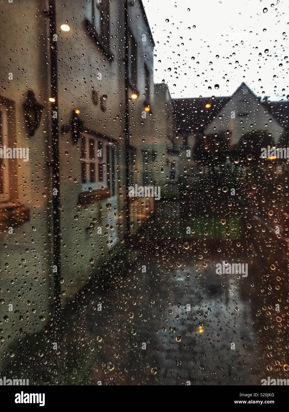 Looking out of a window covered with raindrops, in residential area with lights in the early evening Stock Photo