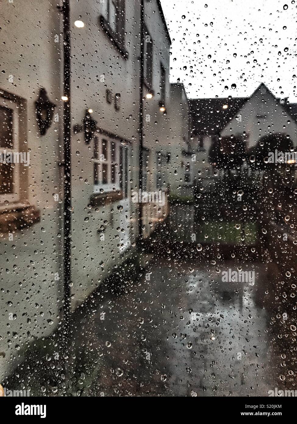 Looking out of a window covered with raindrops, residential area with lights in the early evening Stock Photo