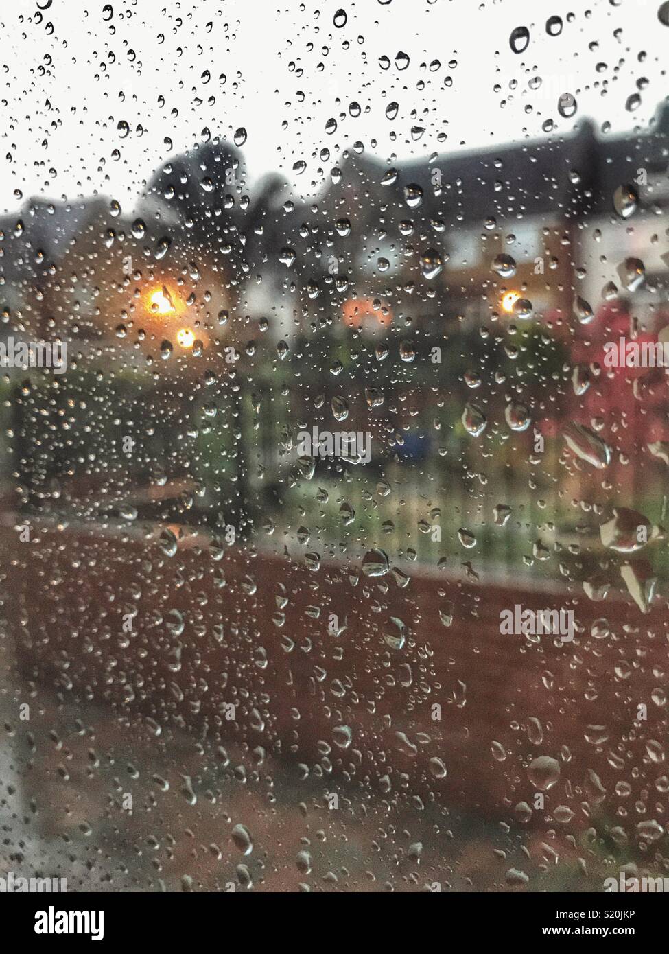 Looking out of a window covered with raindrops, residential area with lights in the early evening - Smartphone Captured Stock Image Looking out of a window covered with raindrops, residential area with lights in the early evening - Smartphone Captured Stock Image