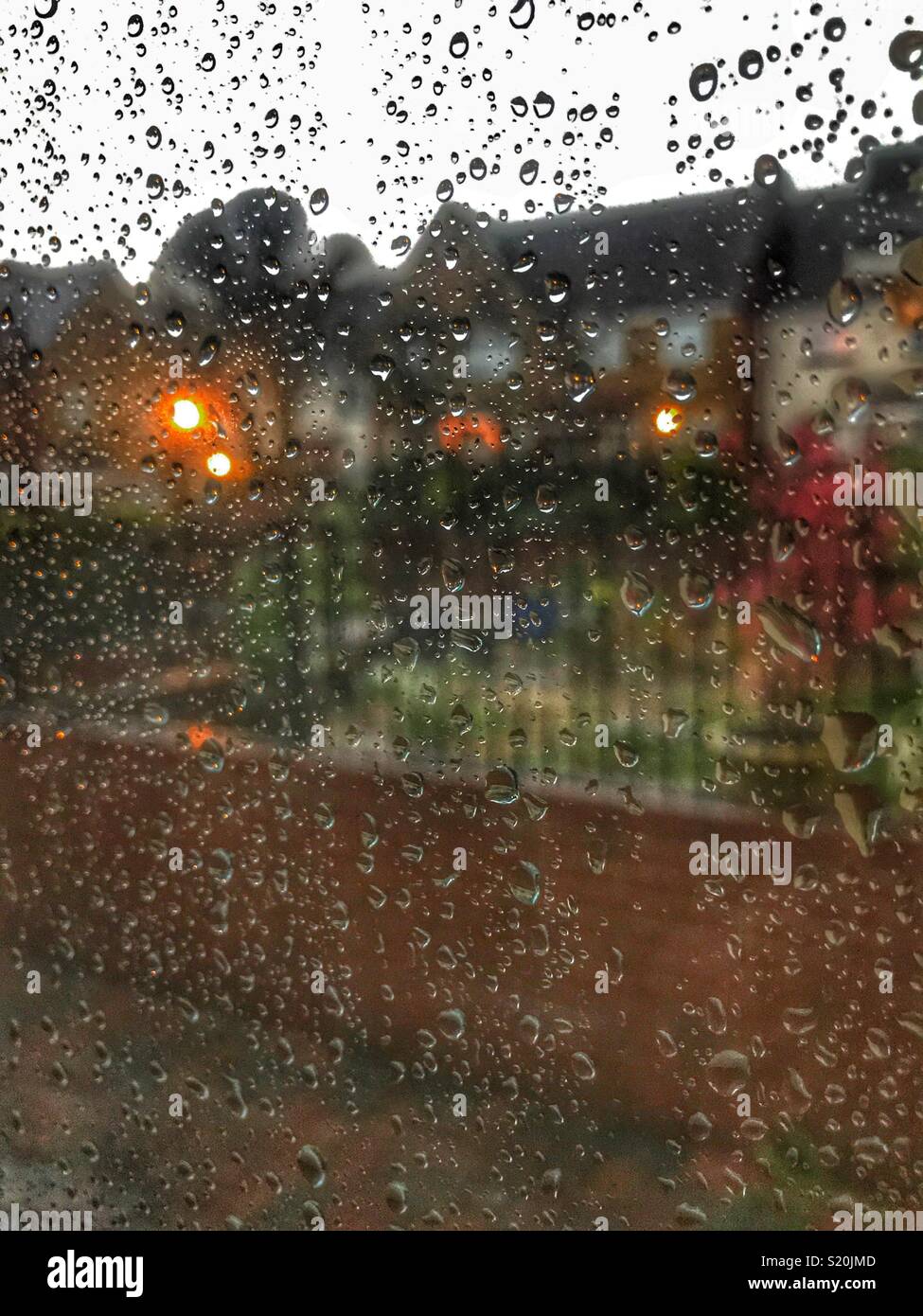 Looking out of a window covered with raindrops, residential area with lights in the early evening - Smartphone Captured Stock Image Looking out of a window covered with raindrops, residential area with lights in the early evening - Smartphone Captured Stock Image