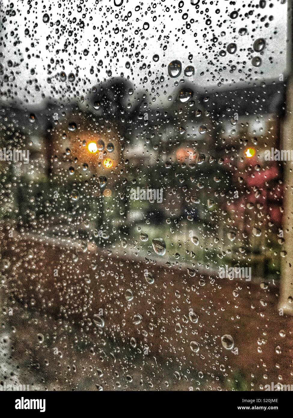 Looking out of a window covered with raindrops, residential area with lights in the early evening - Smartphone Captured Stock Image Looking out of a window covered with raindrops, residential area with lights in the early evening - Smartphone Captured Stock Image