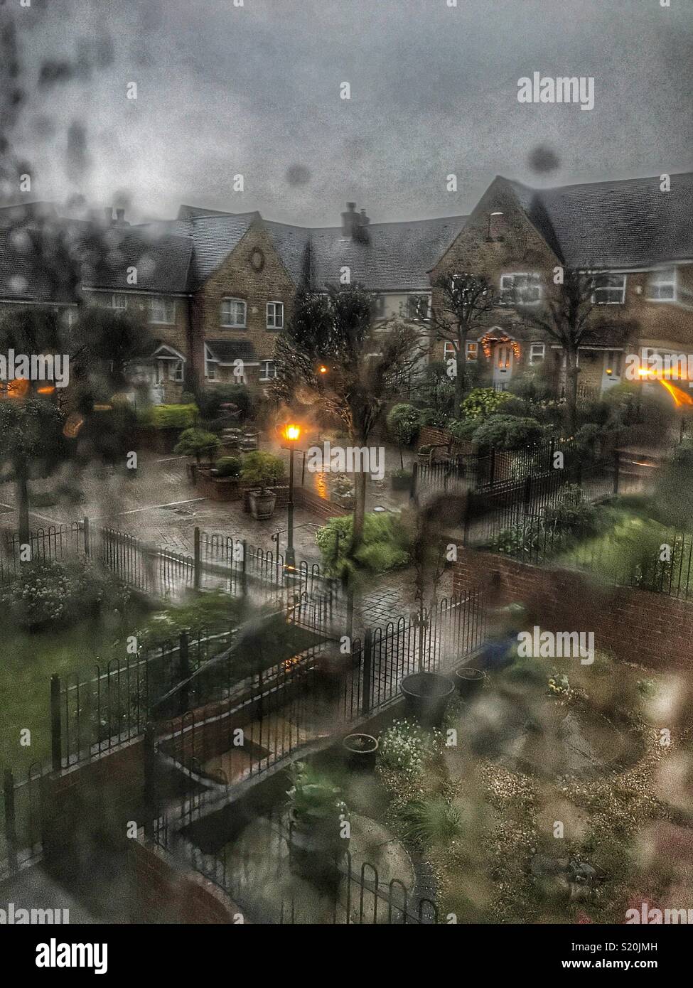 Looking out of a window covered with raindrops, residential area with lights in the early evening Stock Photo