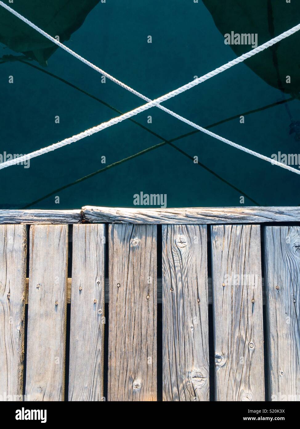 Wooden dock and two ropes over caln blue sea in harbor Stock Photo