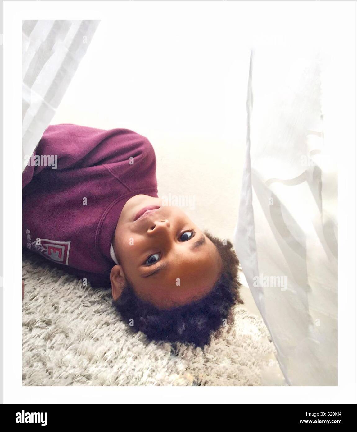 A little boy lies upside down looking at the camera. Stock Photo