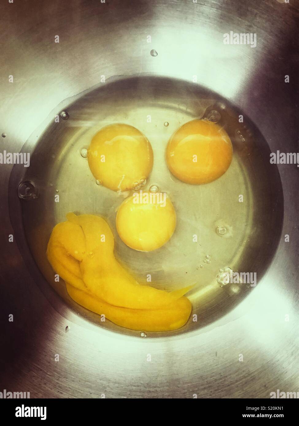 Four cracked eggs in the bottom of a stainless steel bowl that look like a face - Smartphone Captured Stock Image