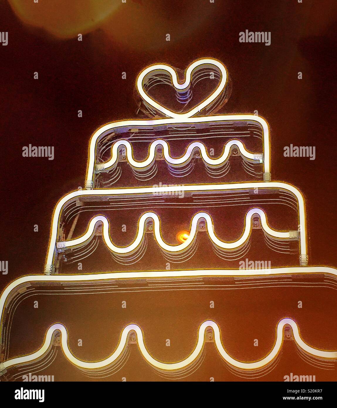 Neon light in the shape of a three layer wedding cake with a heart on top. - Smartphone Captured Stock Image