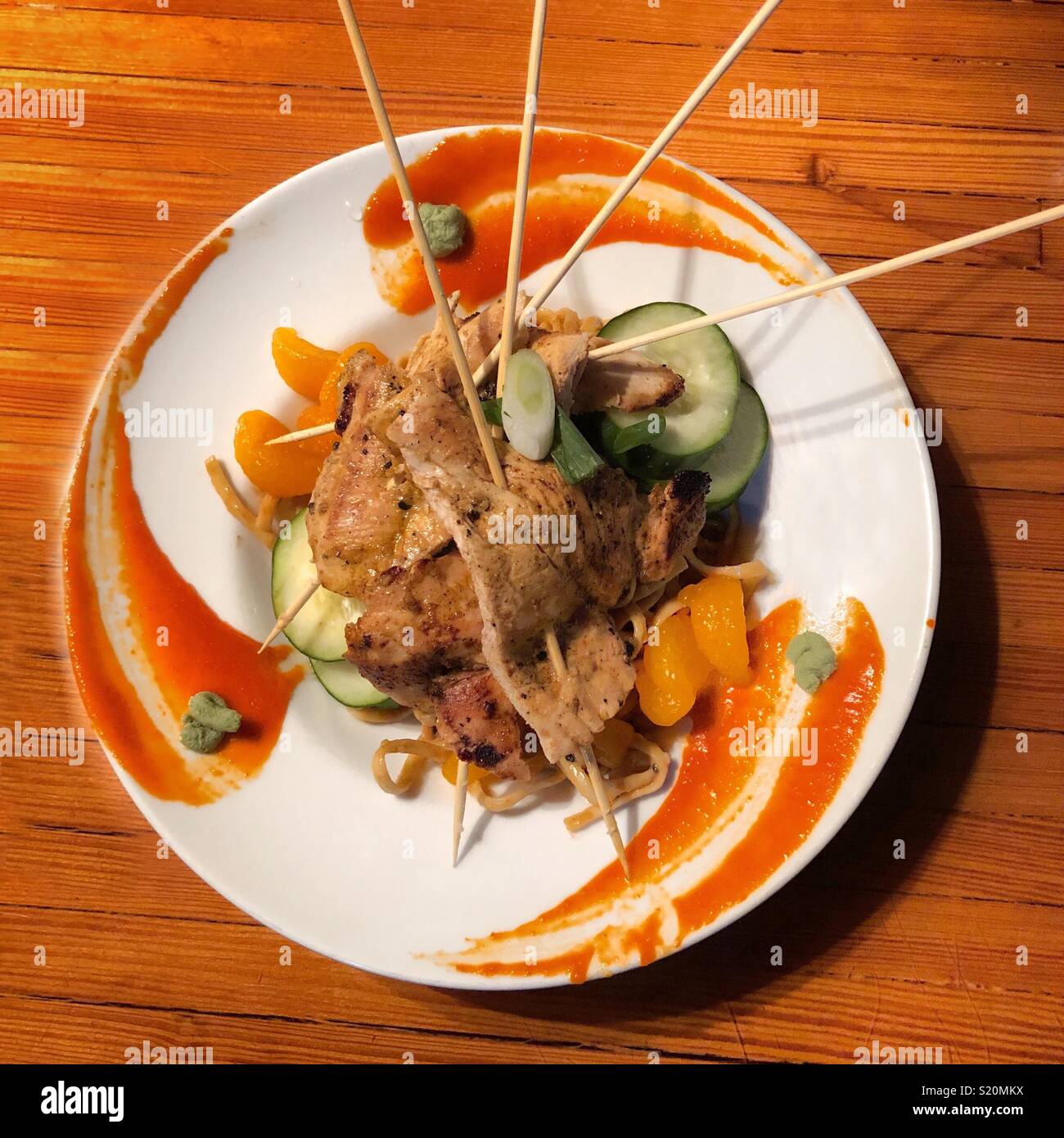 Lemongrass chicken on skewers over a bed of spicy Thai noodles on a round white plate - Smartphone Captured Stock Image