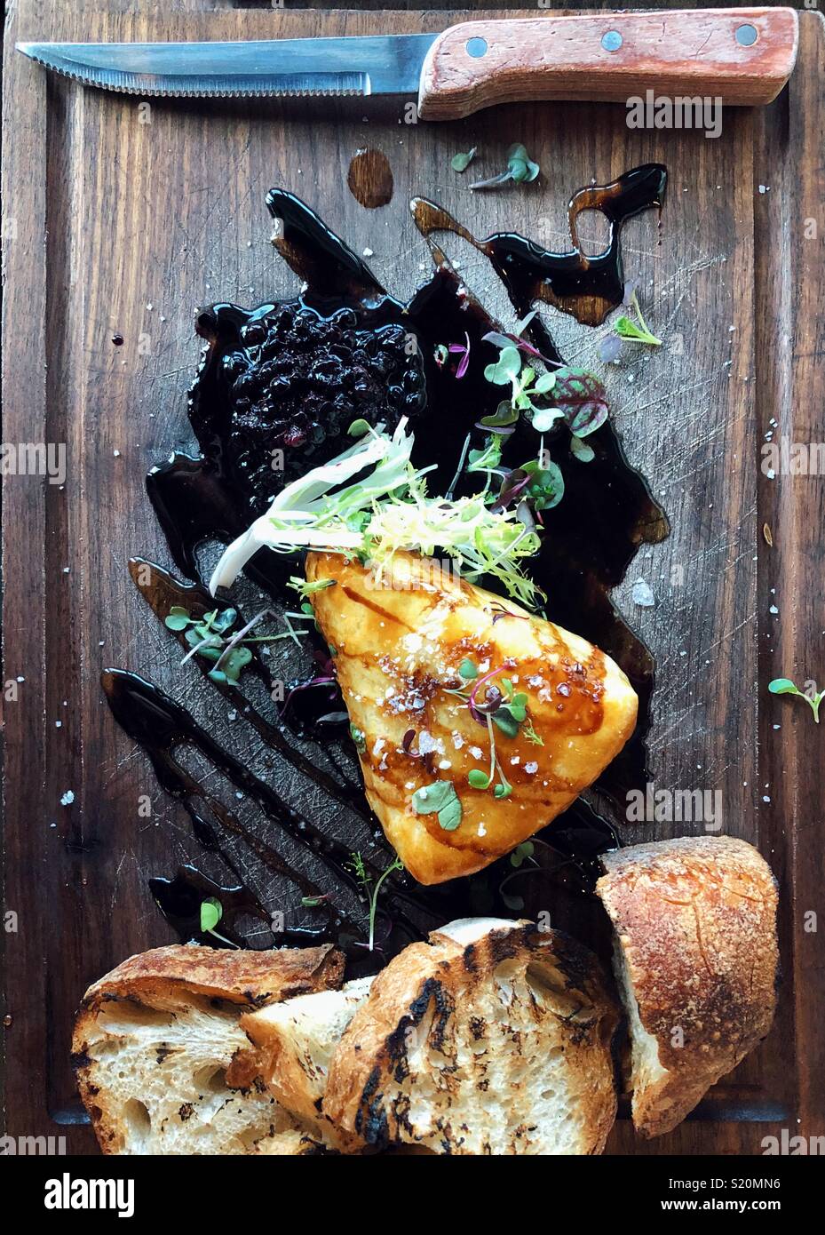Baked brie wedge on a dark wood serving board with toasted bread and wild blueberry compote Stock Photo