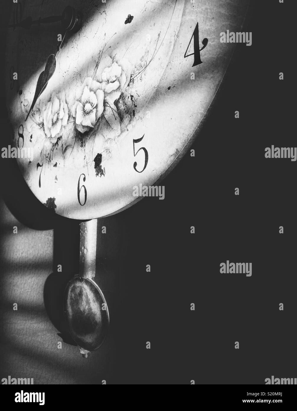 Black and white image of antique style clock with pendulum in morning sunlight through window blinds - Smartphone Captured Stock Image