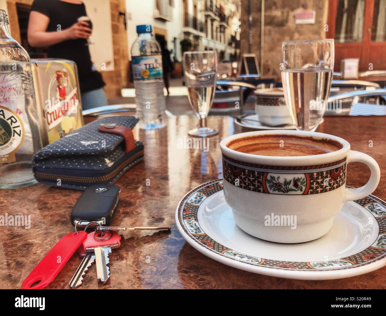 Cup of coffee, cafe con leche, with purse and bunch of keys, on a table at an outdoor cafe, Spain - Smartphone Captured Stock Image