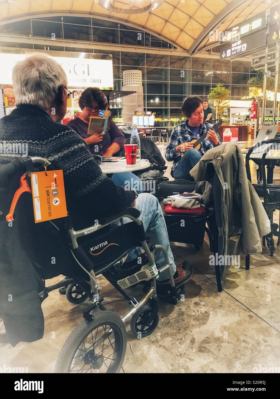 Passengers, including a senior man in a wheelchair, waiting for a delayed flight in the departures area of El Altet airport, Alicante, Spain Stock Photo