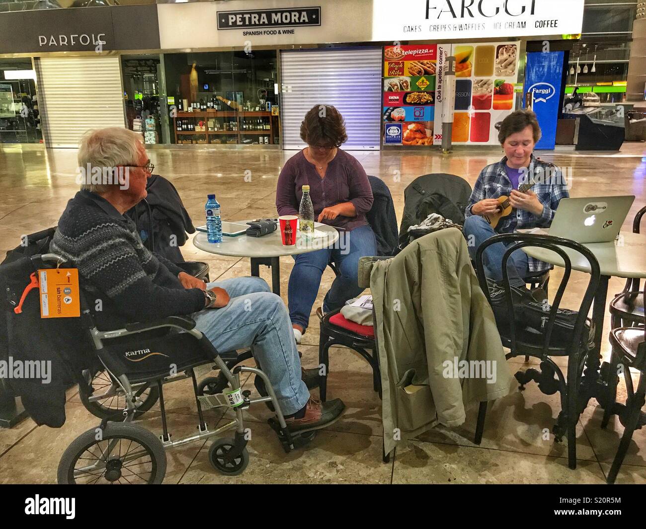Passengers, including a senior man in a wheelchair, waiting for a delayed flight in the departures area of El Altet airport, Alicante, Spain Stock Photo
