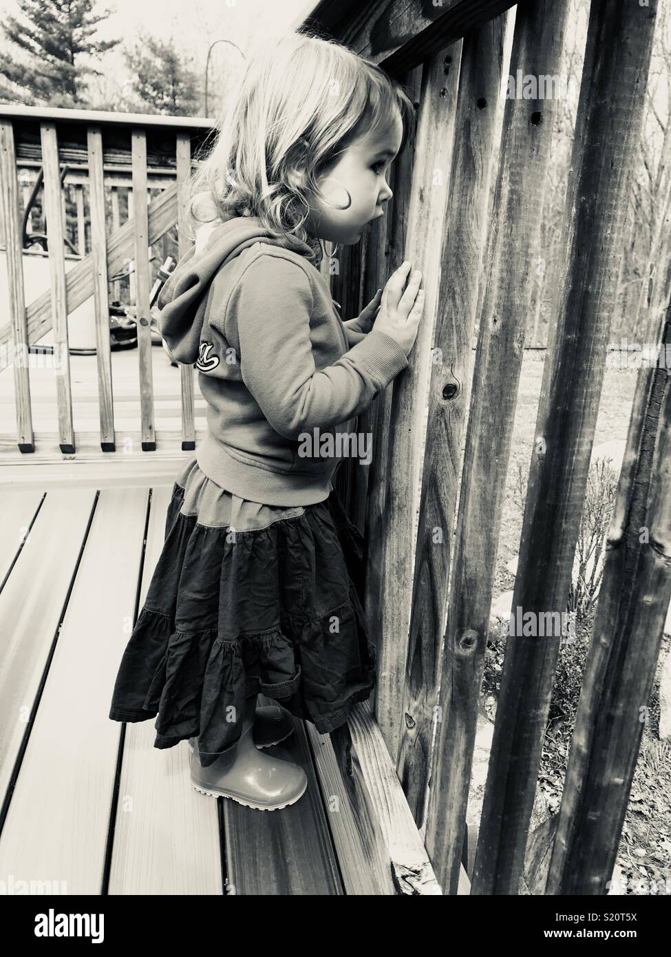 Girl looking through deck fence Stock Photo