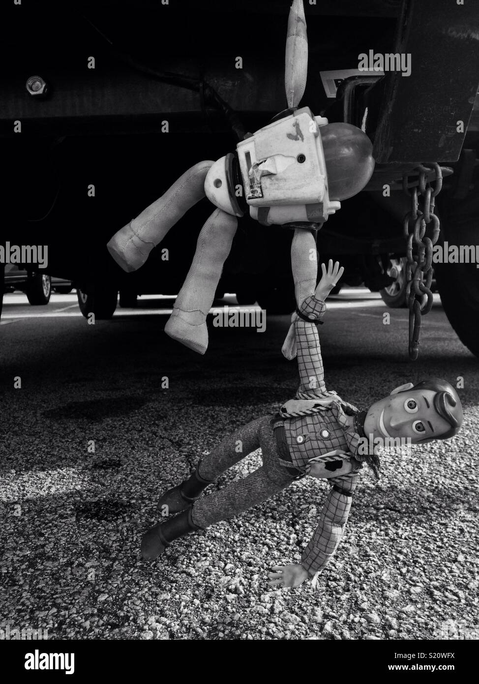 Black and white photo of Buzz Lightyear and Woody hanging from vehicle bumper in North Carolina parking lot Stock Photo