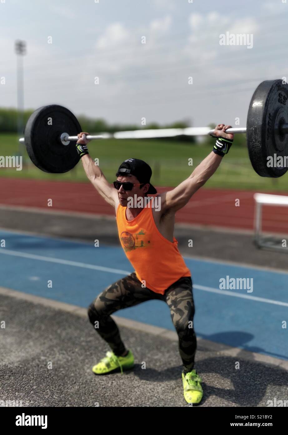 Olympic weightlifter performing a snatch on a sunny day outdoors on an athletics track. Stock Photo