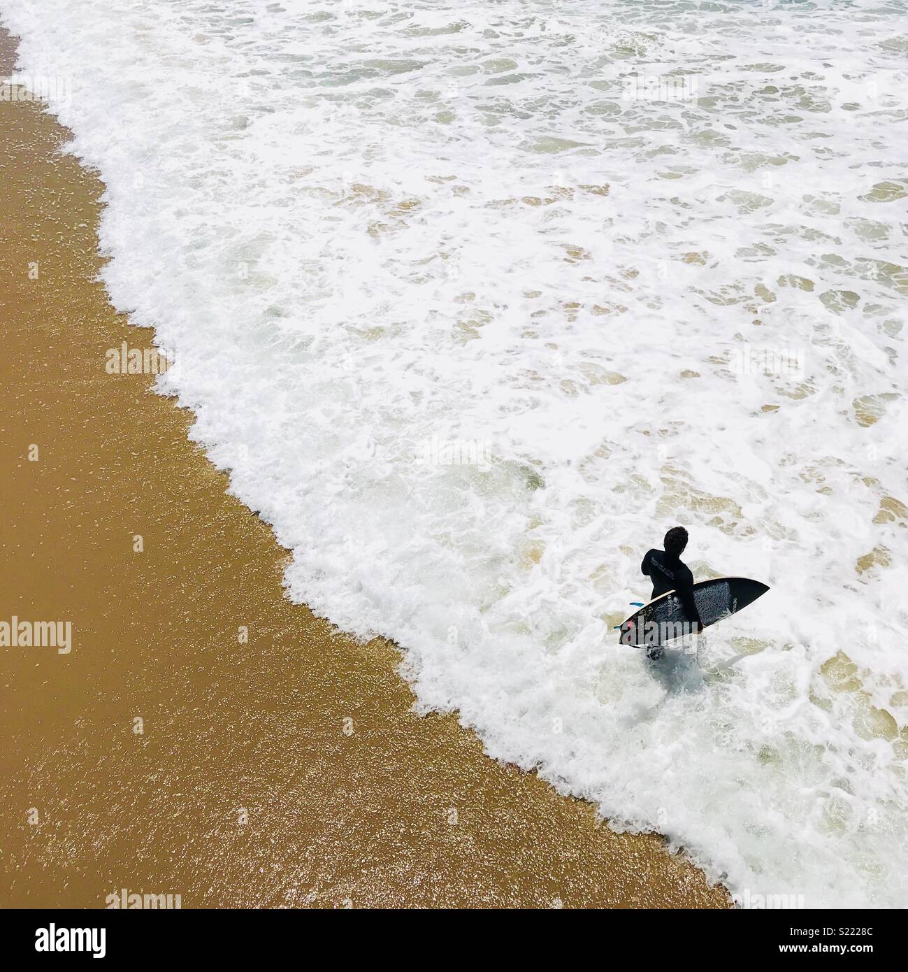 A male surfer walks out into the surf. Manhattan Beach, California USA. Stock Photo