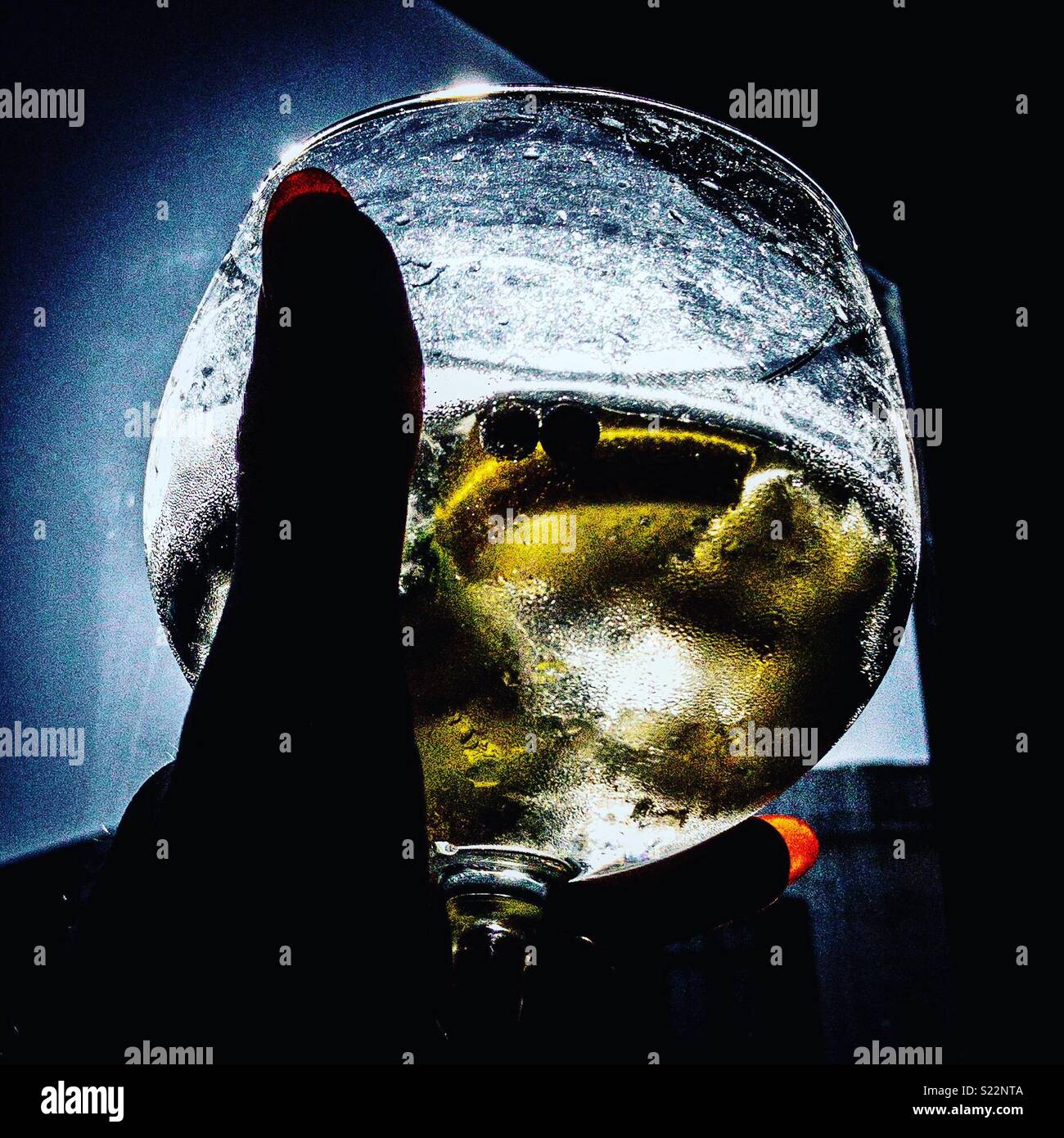 A gin and tonic backlit by the sun held in a female hand - Smartphone Captured Stock Image