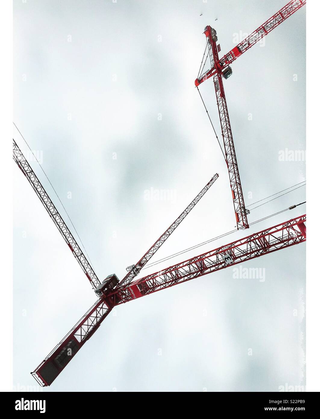 Three red cranes against a grey sky Stock Photo
