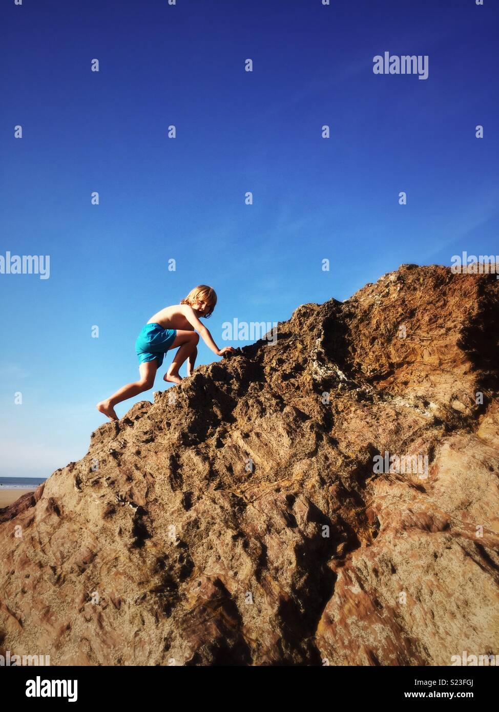 Boy climbing rocks on beach Stock Photo Alamy